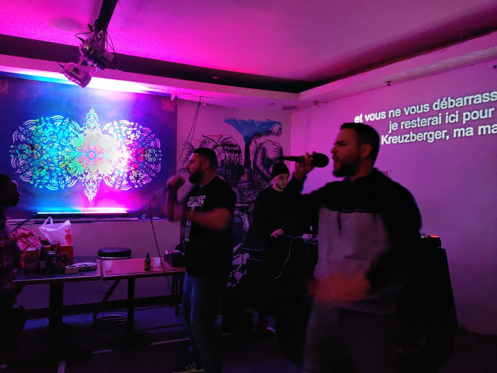 The german Rapper PTK performing in the Aubergine 3000. Behind the translations of his lyrics made by Urbanauth can be percieved, while on the left side a fractalic urban art design by Erwa.One is illuminated in different lights.